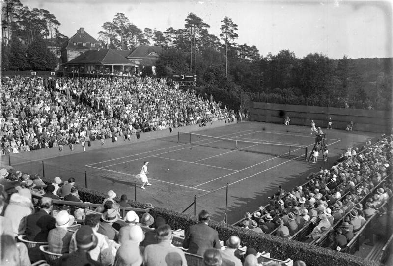 Black-and-white photograph of a packed tennis court in the Grunewald, 1929, spectators on stands around the clay court